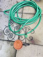 Green garden hose coiled with two wrought iron sconces and terracotta dish