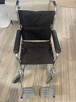 Front view of folding transport wheelchair showing seat, backrest, armrests and footrests
