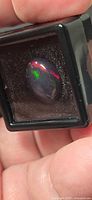 Opal in display box showing dark body tone with bright red and green flashes
