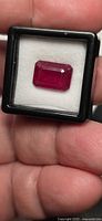 Ruby gemstone in display box held between fingers