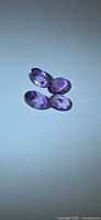 Three oval faceted amethyst gemstones on neutral background