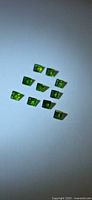 Group of ten square green gemstones on light background