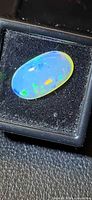 Front view of oval crystal opal in display box showing blue and green play-of-color