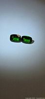 Pair of green cushion-cut gemstones on neutral background