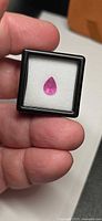 Pear-cut pink sapphire in display box held between fingers