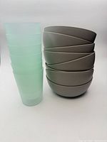 Stacked view of 8 grey bowls and 6 teal tumblers