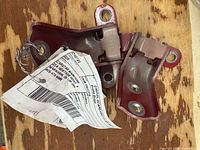 Both red hinge brackets side by side on wood surface with salvage tag attached