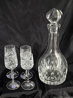 Full view of decanter with stopper and three of the stemmed glasses showing cut pattern
