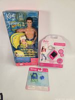 Front view of all three sealed items: Ken & Tommy Swim Buddies boxed set, Barbie B-View keychain blister, Tommy accessory pack blister