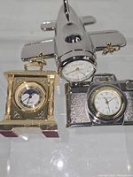 All three novelty desk clocks grouped: gold carriage, chrome camera, chrome airplane