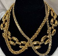 Three gold tone chains draped on black bust showing link styles