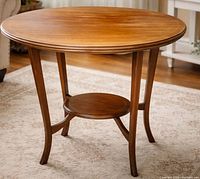 Full view of round wooden accent table showing top, legs, and lower shelf