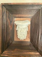 Frontal view of plaster corbel head mounted in wood frame