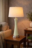 Table lamp lit on side table showing full view of ceramic body, metal base, and linen shade