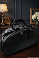 Black leather duffel bag on desk showing full profile, handles, zip closure and luggage tag visible