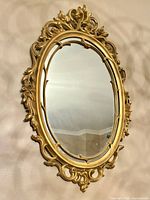 Front angled view showing entire ornate gold oval mirror on wall