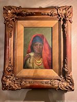 Framed oil portrait of woman wearing red shawl and blue head covering, shown on wall