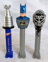 Front view of three PEZ dispensers: Stanley Cup, Batman, NHL goalie mask