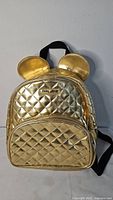 Front view showing quilted gold backpack, Mickey ear panels, logo plate, front zip pocket
