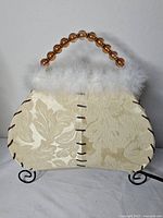 Front view of handbag-shaped lamp showing fabric pattern, fur trim, bead handle, metal stand