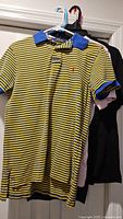 Group of three shirts on hangers: Polo Ralph Lauren striped polo front, pink Nike T-shirt, black T-shirt behind