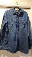 Front view of denim shirt on hanger showing overall style and front pockets