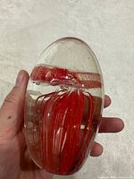 Front view of clear glass paperweight showing red jellyfish inside, hand for scale