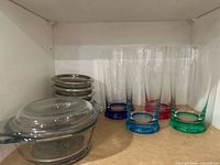 Shelf view showing casserole with lid, stack of coasters, four colored-base tumblers