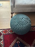 Full view of knitted teal pouf next to sofa