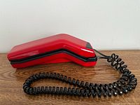 Side view of red angular telephone with black coiled cord