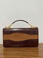 Front view of two-tone crocodile clutch showing gold-tone frame and handle