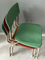 Side view of three stacked fibreglass chairs showing colours and tubular frames