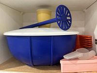 Blue mixing bowl, masher, yellow tumbler, stack of orange coasters, pink pie slice keeper, clear scoop