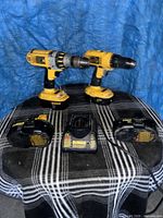Two DeWalt drills, charger and batteries on table