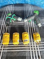 Two black and green garden hose Y splitters and four yellow Hubbell male plugs displayed on plaid surface