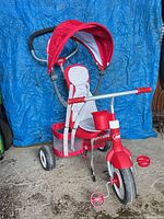 Front view of red Radio Flyer tricycle with canopy, push handle, cup holder, and rear basket visible