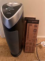 Tower purifier standing next to two boxed filters, power cord visible