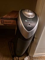 Front view of GermGuardian tower purifier standing upright; sealed replacement filter box visible beside unit