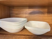 Stack of six larger and three smaller square white bowls on shelf