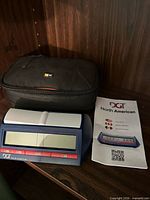 Digital chess clock, carrying case, and instruction manual on shelf
