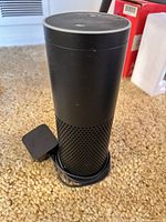 Full view of Amazon Echo speaker standing on carpet with attached power adapter