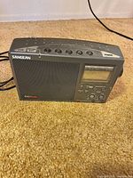 Front view of Sangean CCRadio EX showing speaker, display, controls, attached power cord