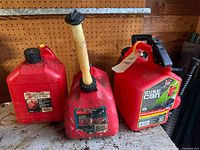 Front view of three red plastic gasoline cans showing labels, spouts and handles