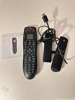 Overall lot showing Logitech Harmony 665 remote with setup guide, Amazon Fire TV Stick dongle, voice remote, and USB cable