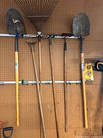 Group of five long-handled garden tools on pegboard