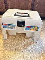 Overall view of Rubbermaid white plastic cleaning shop stool showing handle, latch, and branding
