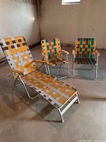 Three vintage aluminum lawn chairs: one chaise lounge, two upright chairs with multicolor webbing