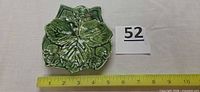 Front view of green majolica leaf plate with strawberries next to ruler for scale