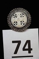 Front view of round brooch showing mother of pearl crosses and decorative silver border