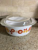 Side view of milk glass casserole with clear lid showing floral motif